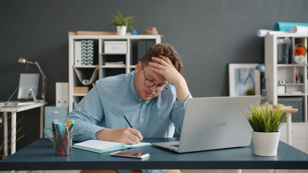 Homem escrevendo na mesa com laptop, parecendo estressado. Homem escrevendo na mesa com laptop, parecendo estressado.