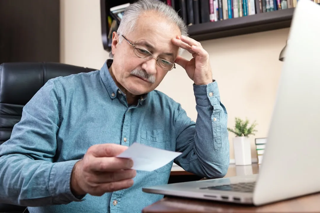 Um homem segurando uma caneta e olhando para um laptop