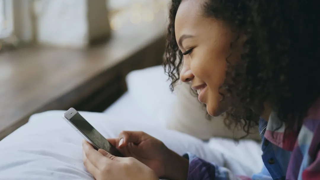 Jovem sorrindo enquanto usa seu smartphone na cama. Jovem sorrindo enquanto usa seu smartphone na cama.